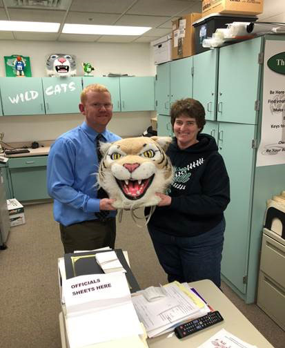 Darren Kobliska, history teacher, passes the Wildcat head to Darlene Castillo, athletic secretary. 