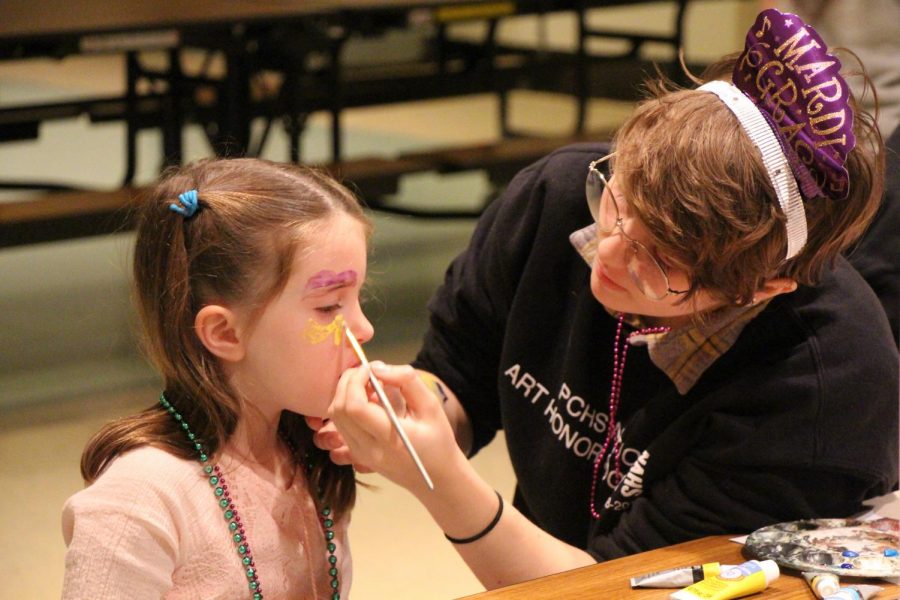 Junior Julia Jessen volunteers at the face painting station for National Art Honor Society at the Mardi Gras celebration in the cafeteria on Tuesday, March 5th. 