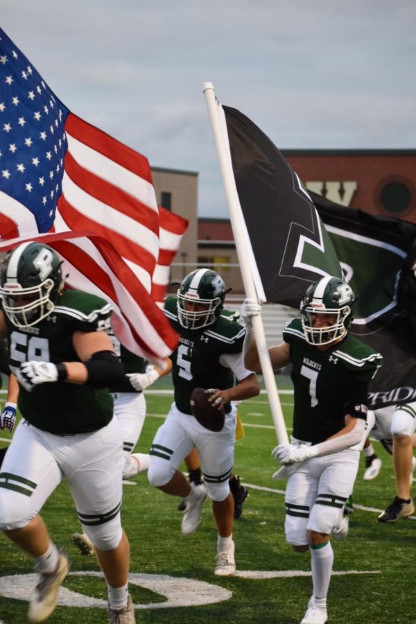 The varsity team is welcomed with cheers as they start the game on Sept 6. James Buck, senior, can be seen carrying the football onto the field.