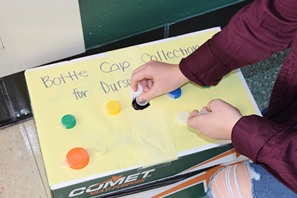 A student donates a bottle cap into the donation box in the front foyer.