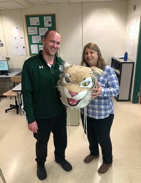 Bev Jakubiak, teaching assistant, passes the Wildcat Award to Ken Schoen, computer teacher.